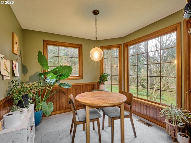 dining area with a wealth of natural light, a wainscoted wall, visible vents, and wooden walls