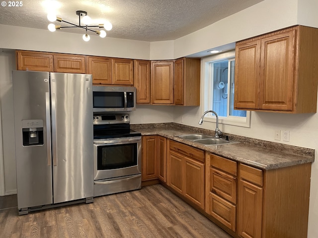 kitchen with appliances with stainless steel finishes, sink, dark wood-type flooring, a textured ceiling, and an inviting chandelier