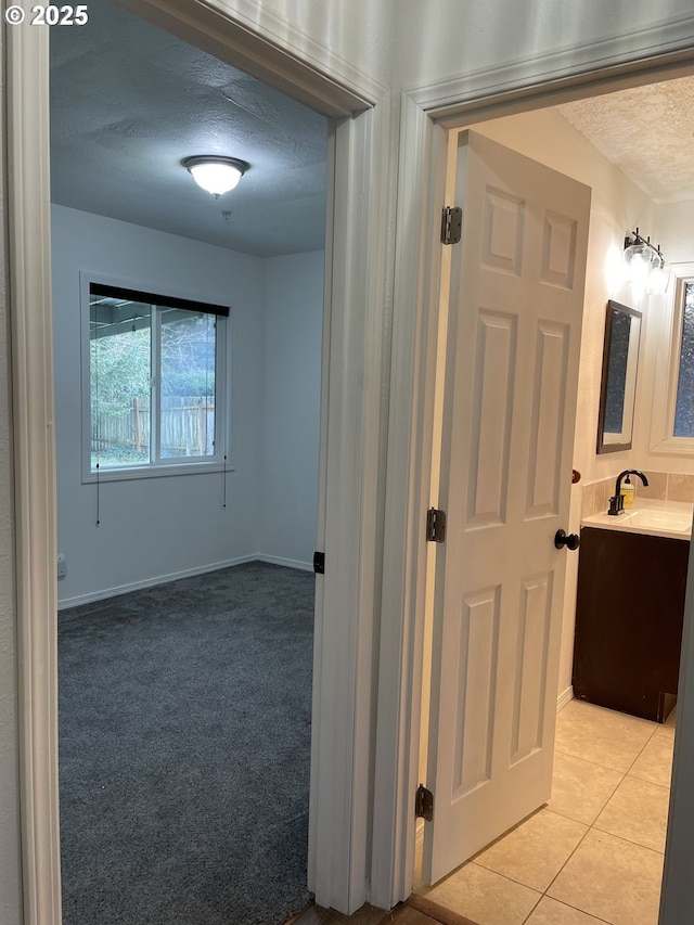 hall with sink, a textured ceiling, and light tile patterned floors