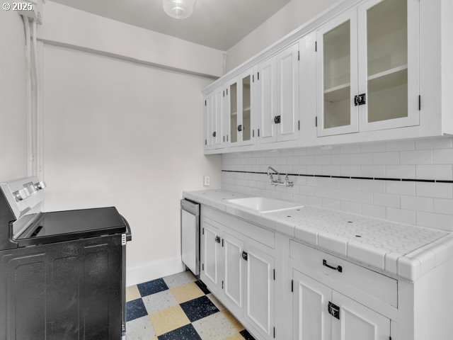 20 NW 16th Ave Unit 8, Portland, OR 97209 - kitchen featuring backsplash, washer / clothes dryer, a sink, light floors, and white cabinetry