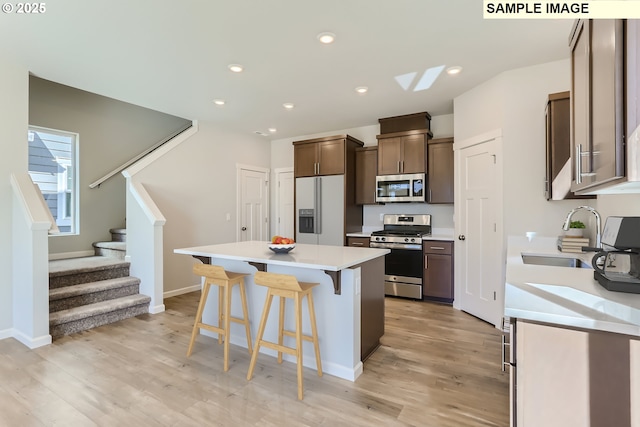 kitchen featuring appliances with stainless steel finishes, a sink, a kitchen bar, a kitchen island, and light countertops