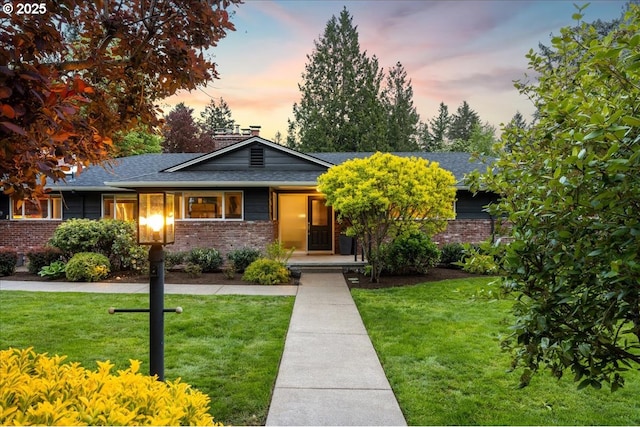 view of front of property featuring brick siding, a shingled roof, and a front lawn