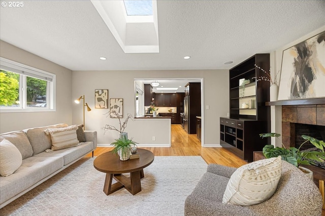 living area featuring a textured ceiling, a skylight, a tile fireplace, light wood finished floors, and recessed lighting