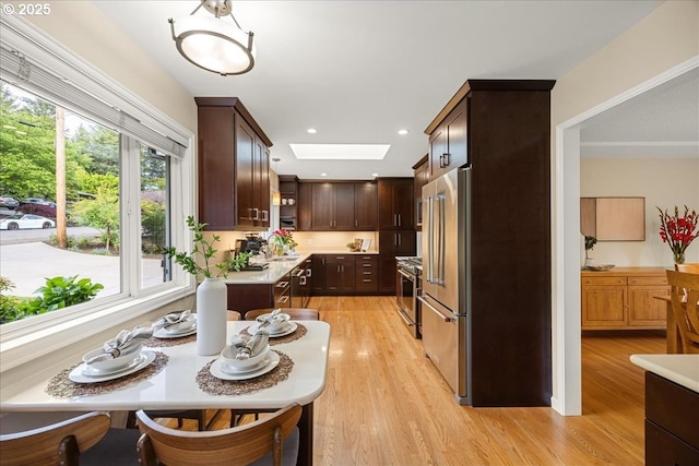 kitchen featuring light countertops, high end appliances, a skylight, and dark brown cabinets