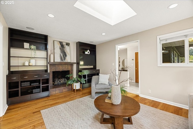 living area with baseboards, a skylight, wood finished floors, and a fireplace