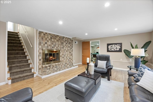 living area featuring stairs, a tile fireplace, baseboards, recessed lighting, and light wood-style flooring