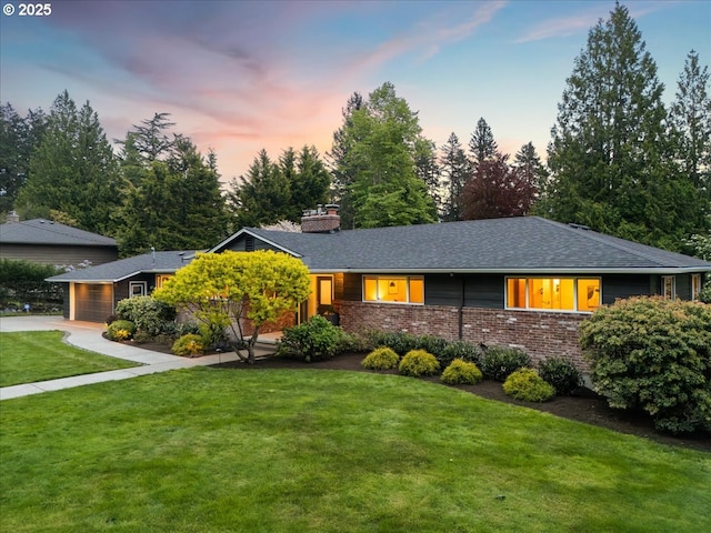 view of front of house with roof with shingles, a chimney, a yard, and brick siding