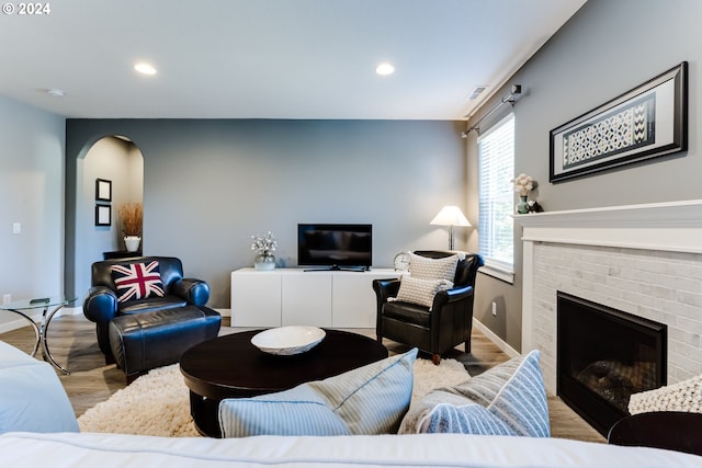 living area featuring wood finished floors, a fireplace, arched walkways, recessed lighting, and baseboards