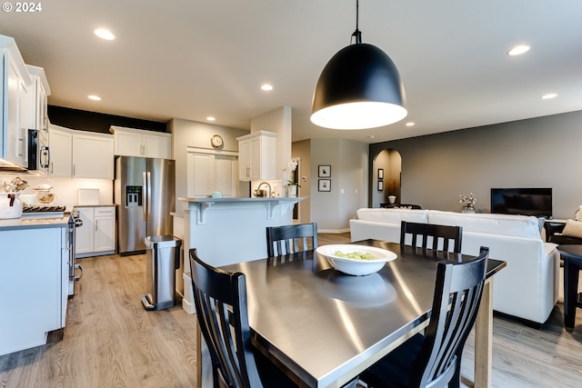 dining area with light wood-style flooring, arched walkways, and recessed lighting