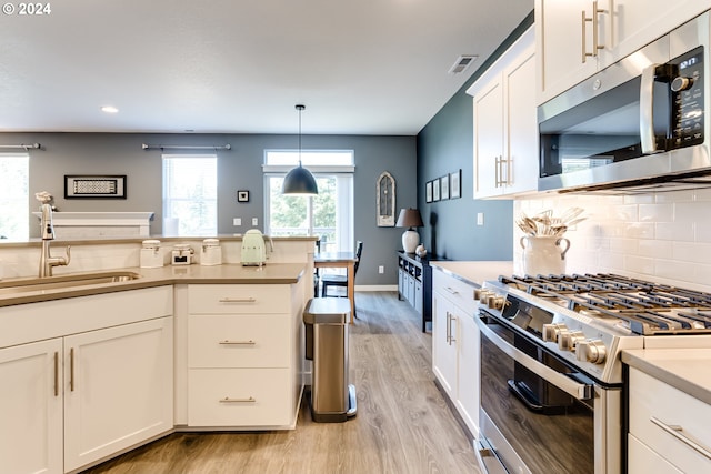 kitchen featuring stainless steel appliances, light wood-style floors, a sink, tasteful backsplash, and light countertops