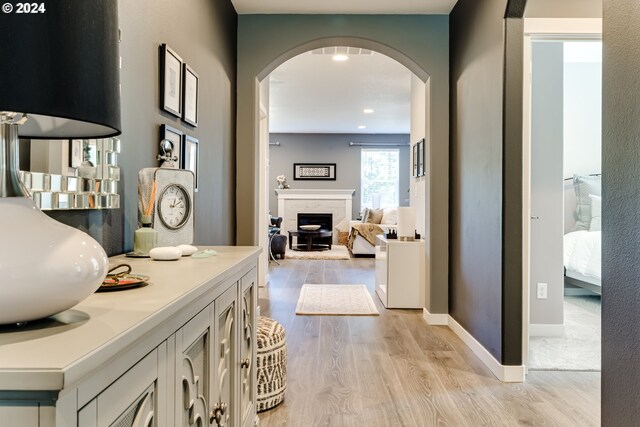 hallway featuring arched walkways, light wood-type flooring, and baseboards