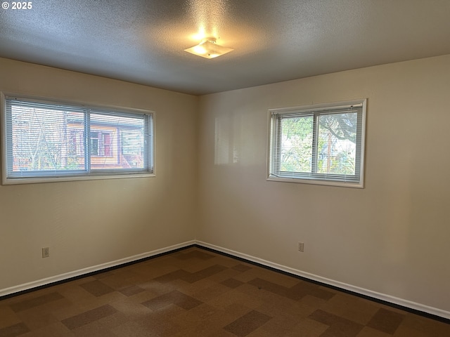 spare room featuring dark carpet, a textured ceiling, and a wealth of natural light