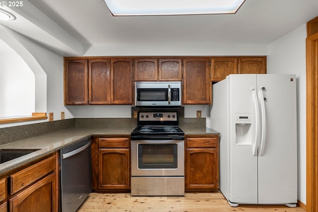 kitchen with appliances with stainless steel finishes, light wood-style floors, dark countertops, and brown cabinets
