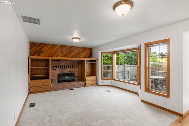 unfurnished living room featuring baseboards, carpet floors, wooden walls, a brick fireplace, and a textured ceiling