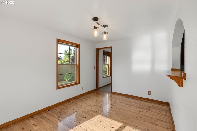spare room with arched walkways, hardwood / wood-style floors, and baseboards
