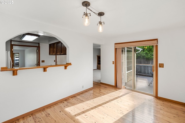 unfurnished room with light wood-style flooring, arched walkways, and baseboards