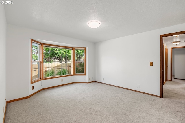 unfurnished room with light colored carpet, baseboards, and a textured ceiling