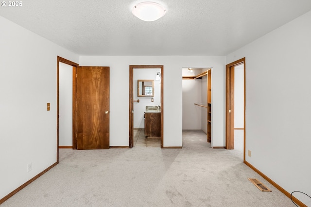 unfurnished bedroom featuring a spacious closet, light colored carpet, a textured ceiling, ensuite bathroom, and a closet