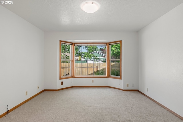 empty room featuring light carpet, baseboards, and a textured ceiling