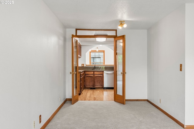 spare room featuring a sink, light carpet, baseboards, french doors, and a textured ceiling