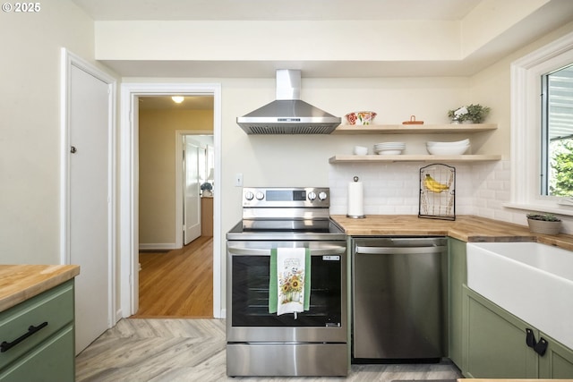 2535 N Baldwin St, Portland, OR 97217 - kitchen featuring green cabinetry, stainless steel appliances, wall chimney exhaust hood, wood counters, and decorative backsplash