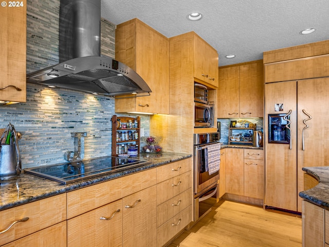 89610 Sea Breeze Dr, Warrenton, OR 97146 - kitchen with dark stone countertops, wall chimney exhaust hood, backsplash, light wood-style floors, and stainless steel appliances