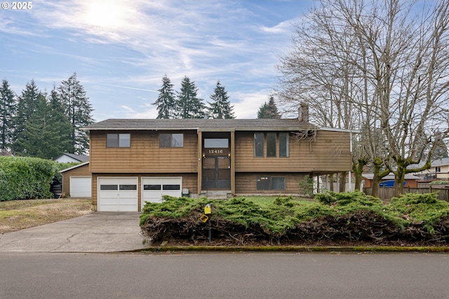 split foyer home featuring a garage, concrete driveway, a chimney, and fence