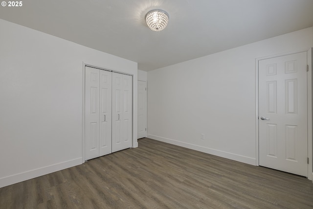 unfurnished bedroom with baseboards, a notable chandelier, dark wood-style floors, and a closet