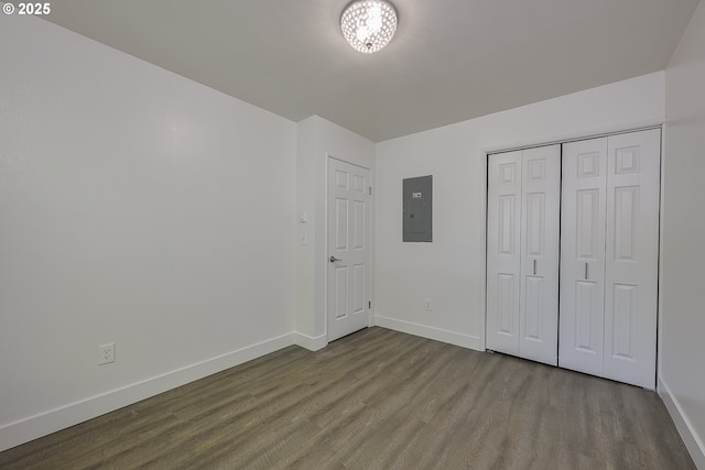 unfurnished bedroom with a closet, baseboards, wood finished floors, and electric panel