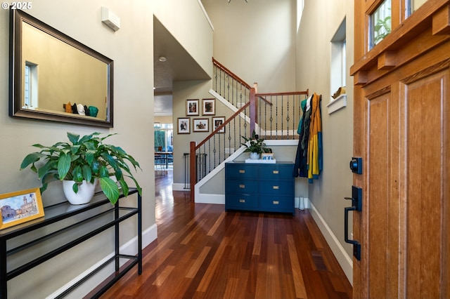 foyer entrance featuring stairway, baseboards, dark wood finished floors, and a towering ceiling