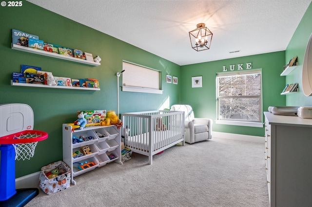 carpeted bedroom featuring a nursery area, a chandelier, baseboards, and a textured ceiling