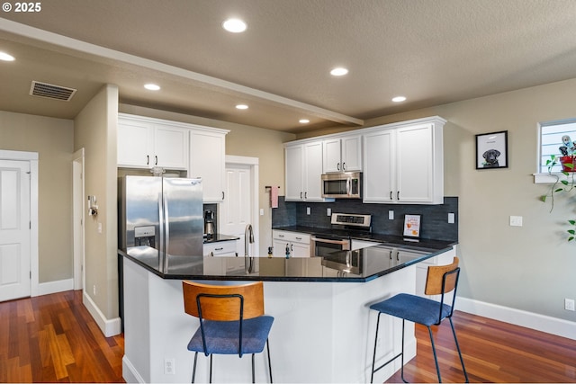 kitchen with visible vents, a breakfast bar, stainless steel appliances, white cabinetry, and backsplash