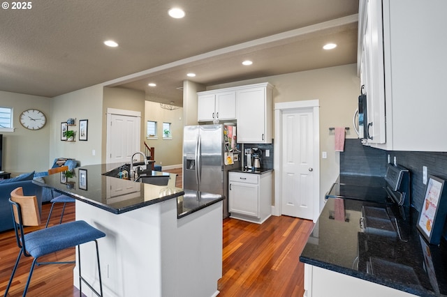 kitchen with a sink, appliances with stainless steel finishes, dark wood-style flooring, tasteful backsplash, and a breakfast bar area