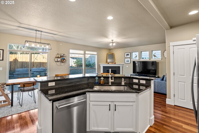 kitchen with a sink, stainless steel dishwasher, open floor plan, dark wood-style flooring, and a textured ceiling