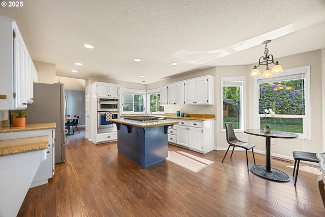 8967 SW Leslie St, Portland, OR 97223 - kitchen featuring appliances with stainless steel finishes, a center island, white cabinetry, dark wood-type flooring, and a textured ceiling