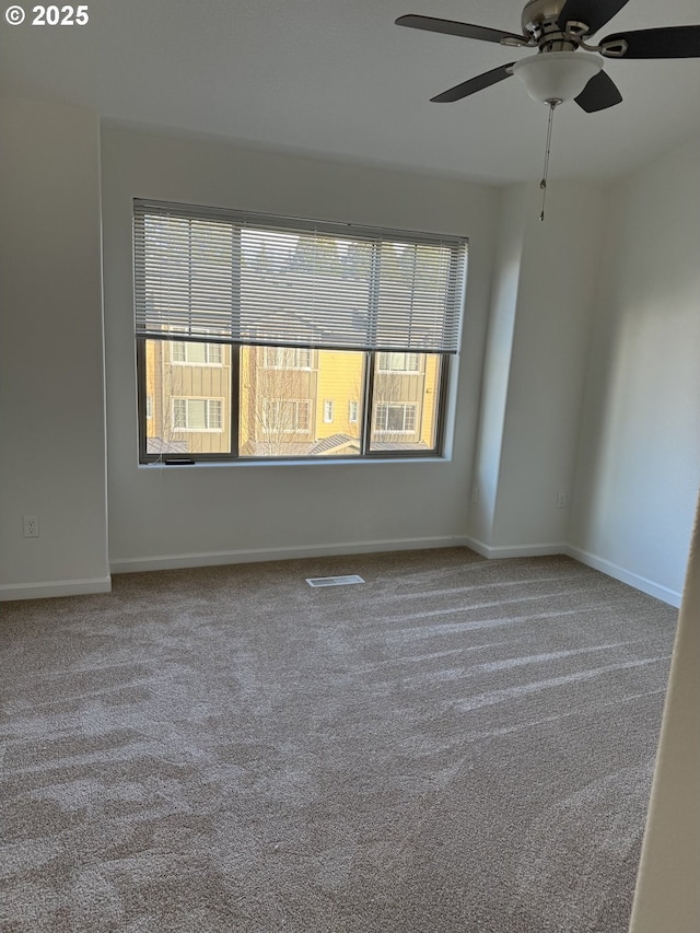 empty room with a ceiling fan, carpet flooring, visible vents, and baseboards