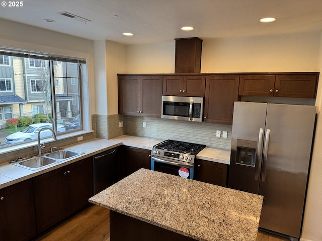 kitchen featuring light stone counters, stainless steel appliances, a sink, dark brown cabinets, and tasteful backsplash