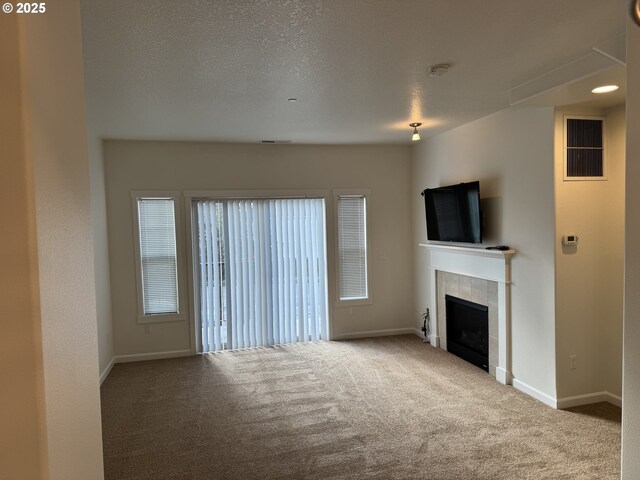 unfurnished living room featuring carpet floors, visible vents, a tiled fireplace, a textured ceiling, and baseboards