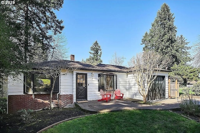 rear view of property with brick siding, a chimney, a yard, a patio area, and an attached garage