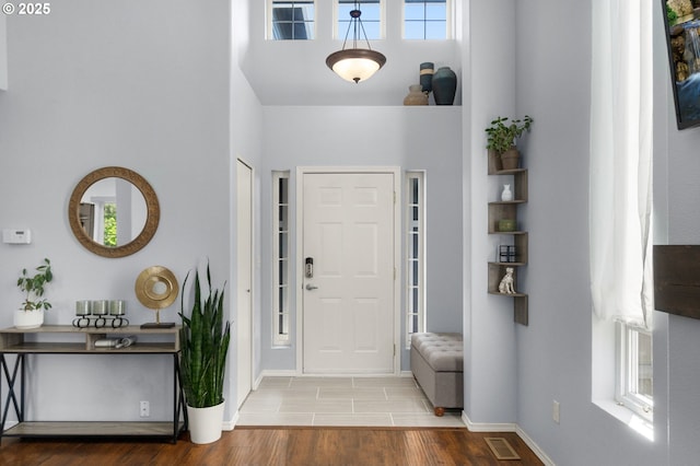 foyer entrance with visible vents, a high ceiling, baseboards, and wood finished floors