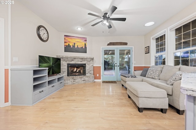 living room with french doors, ceiling fan, built in features, a fireplace, and light hardwood / wood-style floors