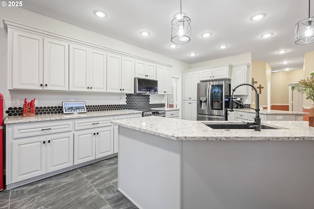 kitchen with stainless steel appliances, a kitchen island with sink, sink, pendant lighting, and white cabinets