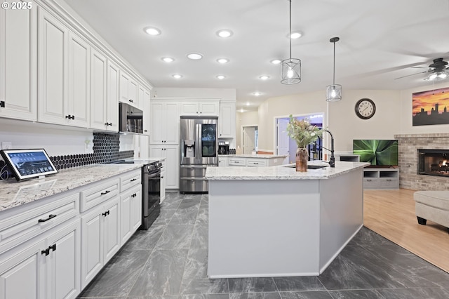 kitchen with light stone countertops, stainless steel appliances, decorative light fixtures, a center island with sink, and white cabinets