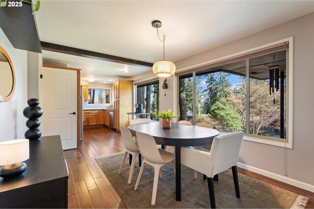 dining area featuring beam ceiling, dark wood-style floors, and baseboards