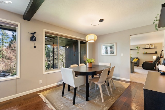 dining space with dark wood finished floors, beamed ceiling, plenty of natural light, and baseboards