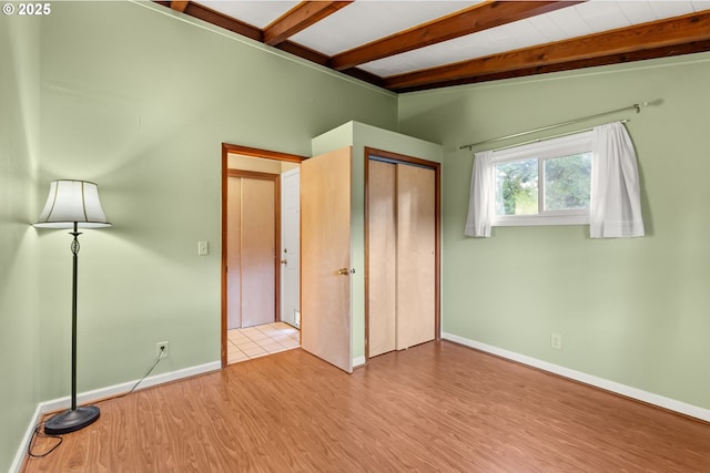 unfurnished bedroom featuring vaulted ceiling with beams, light wood-type flooring, and a closet