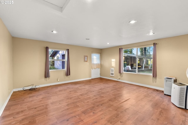 spare room with heating unit, light hardwood / wood-style floors, and a healthy amount of sunlight