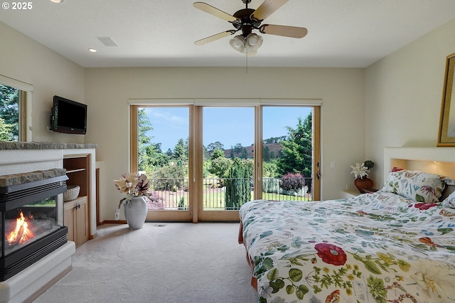 bedroom featuring a glass covered fireplace, multiple windows, light carpet, and access to exterior