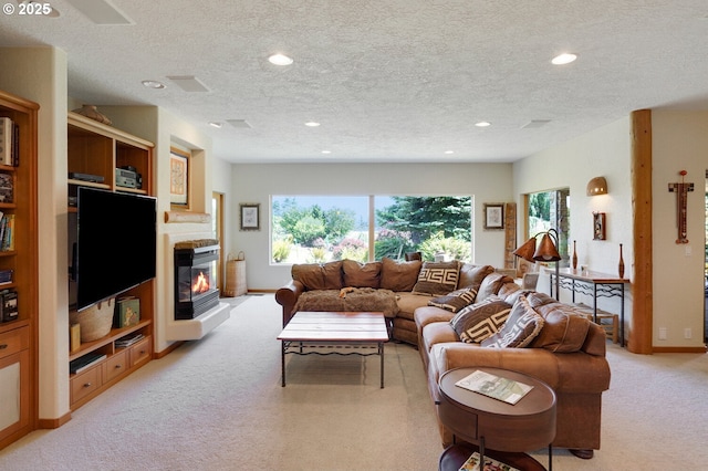 living room with light colored carpet, recessed lighting, a textured ceiling, and a glass covered fireplace