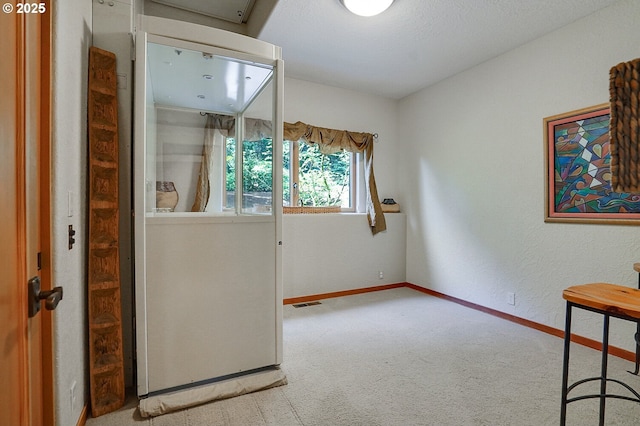 interior space with baseboards, carpet, a textured wall, and visible vents